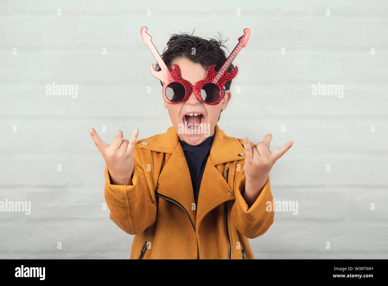 Enfant avec des lunettes faisant symbole rock avec les mains à fond brique Banque D'Images