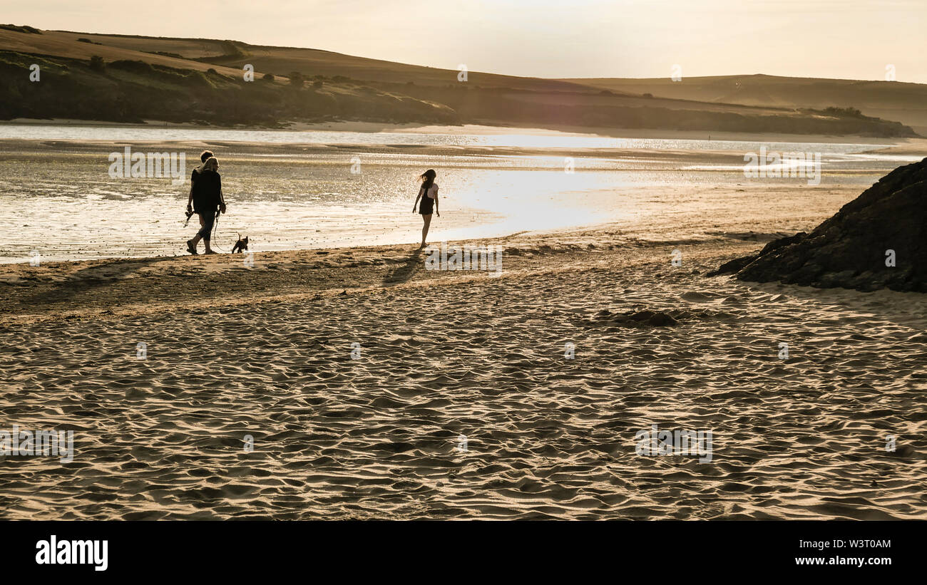 Une famille de trois personnes et un chien à marcher le long de la mer avec le soleil du soir sur l'estuaire de Camel à marée basse en Cornouailles du Nord. Banque D'Images