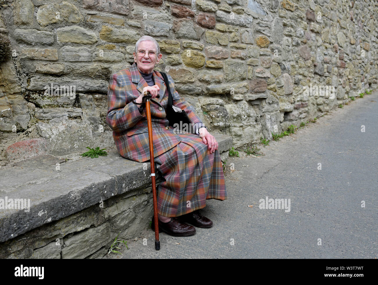 Femme âgée assise sur le siège de pierre en prenant un repos bien mérité sur la montée raide dans Ludlow Banque D'Images