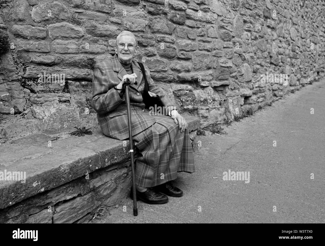 Femme âgée assise sur le siège de pierre en prenant un repos bien mérité sur la montée raide dans Ludlow Banque D'Images