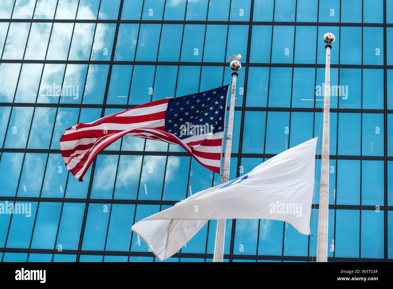 Waving American Stars and Stripes drapeau avec le centre-ville de capacités reflétant Ciel et nuages en arrière-plan. Banque D'Images