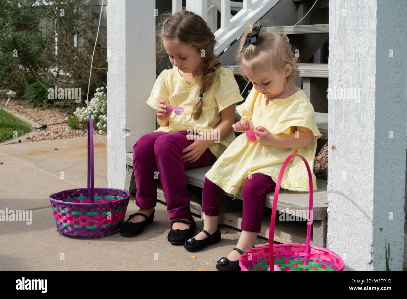 Deux filles de race blanche, 2 ans et 5 ans, s'asseoir sur les escaliers et ouvrir les oeufs de Pâques en plastique et manger traite d'eux. USA Banque D'Images