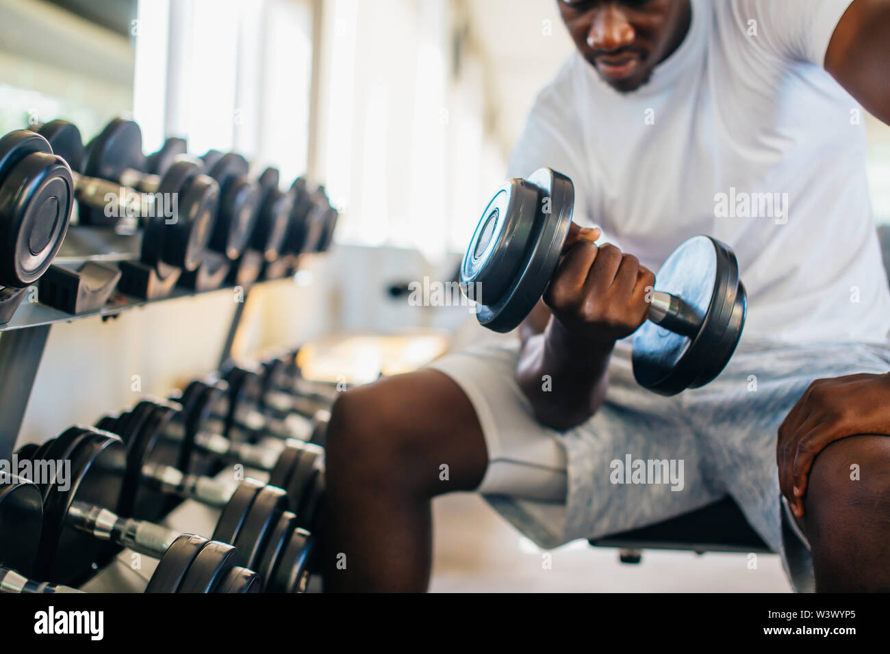 Young African American man et levage un haltère près de la grille à une salle de sport. La formation de poids mâle personne faisant un biceps curl dans le centre de remise en forme Banque D'Images