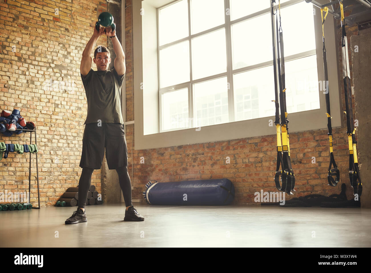 Ce corps parfait. Forte de pleine longueur et bel homme holding big haltère noir sous sa tête tandis que l'exercice à la salle de sport. Des exercices de poids corporel. Concept de culturisme. D'entraînement. Banque D'Images