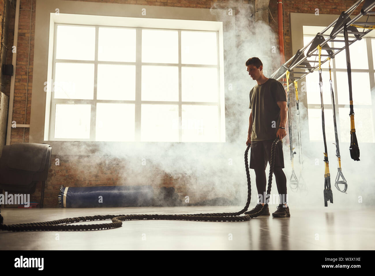 Ne jamais s'arrêter. Vue latérale du jeune homme athlétique avec corps parfait faisant des exercices crossfit avec une corde dans la salle de sport. Formation CrossFit. Sport concept Banque D'Images