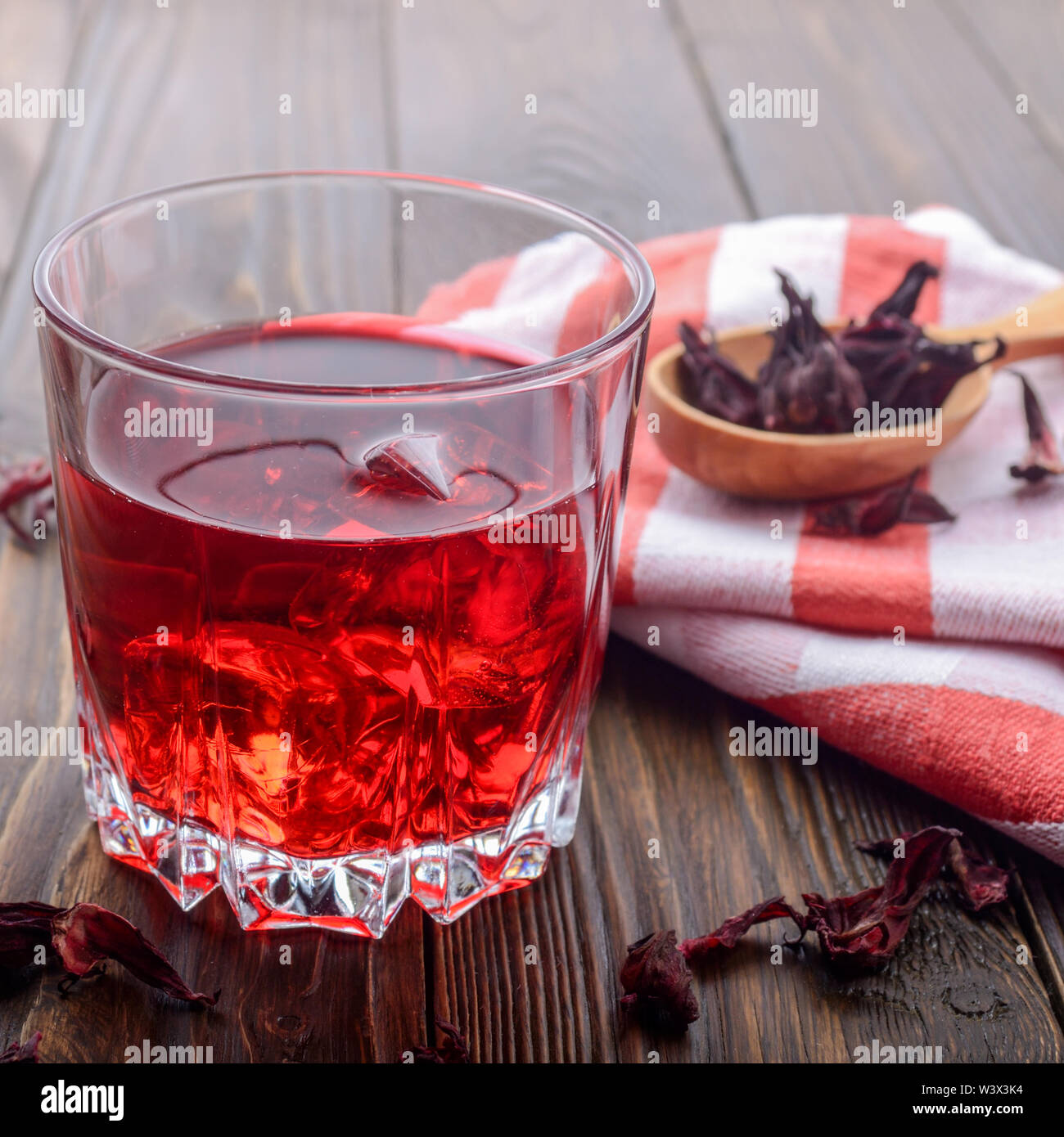 Vue rapprochée au verre de thé avec de la glace et la cuillère de pétales d'hibiscus à sec sur fond de table en bois Banque D'Images