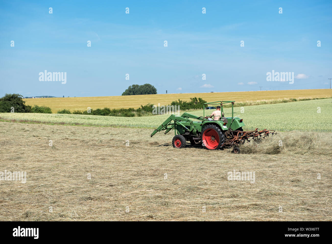 Farmer le tracteur tourne l'herbe pour un meilleur séchage à façon Banque D'Images