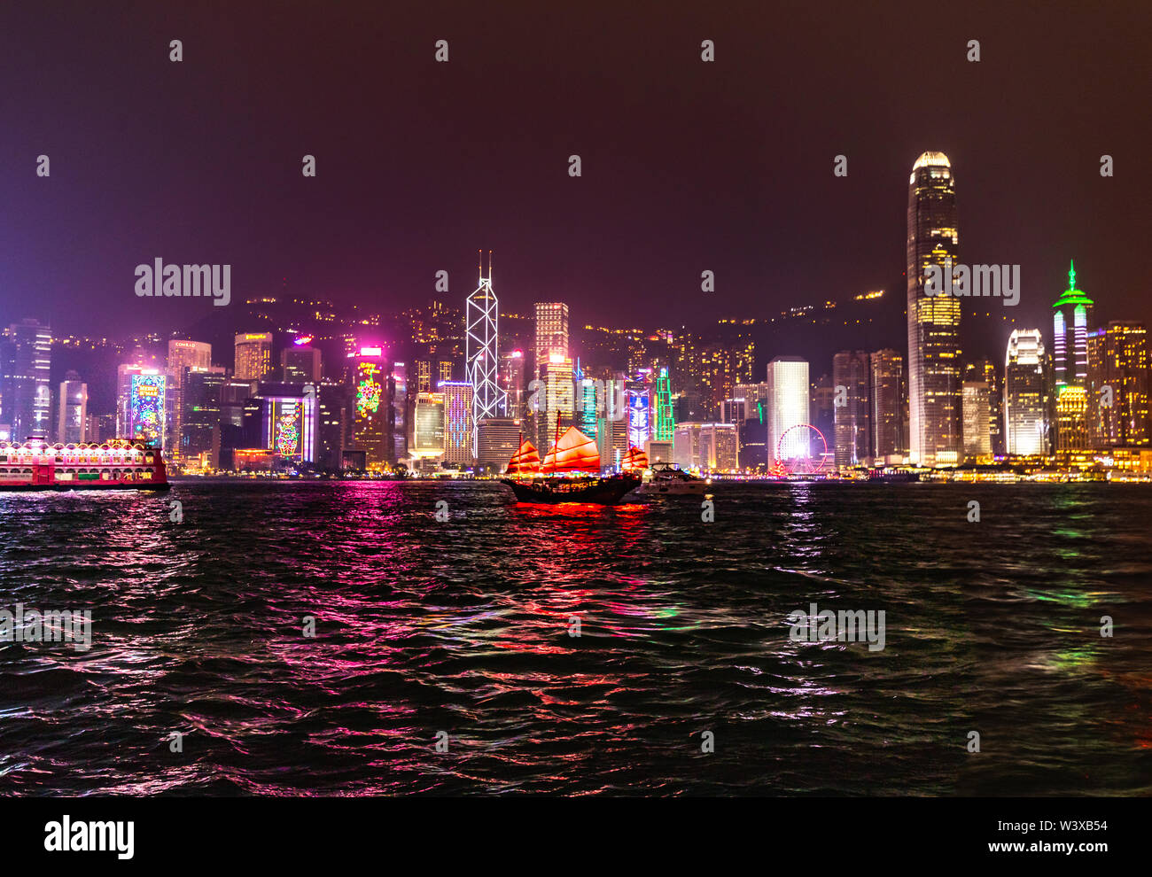 Vue sur la ville avec gratte-ciel avec bateau à voile rouge au port de Hong Kong la nuit Banque D'Images