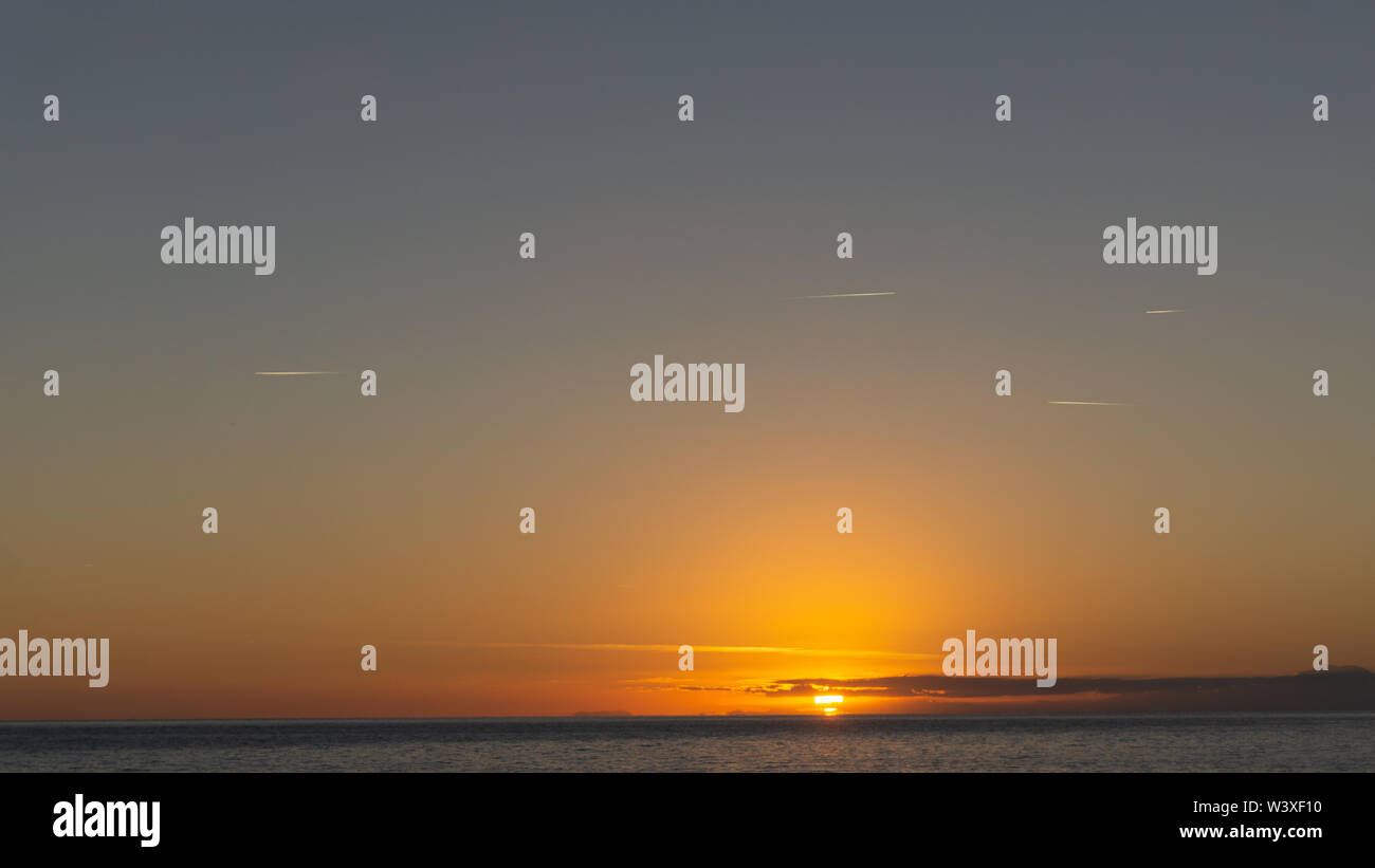 Coucher de soleil avec des sentiers de l'avion dans le ciel. Très faible soleil sur l'horizon. Banque D'Images Coucher de soleil avec des sentiers de l'avion dans le ciel. Très faible soleil sur l'horizon. Banque D'Images