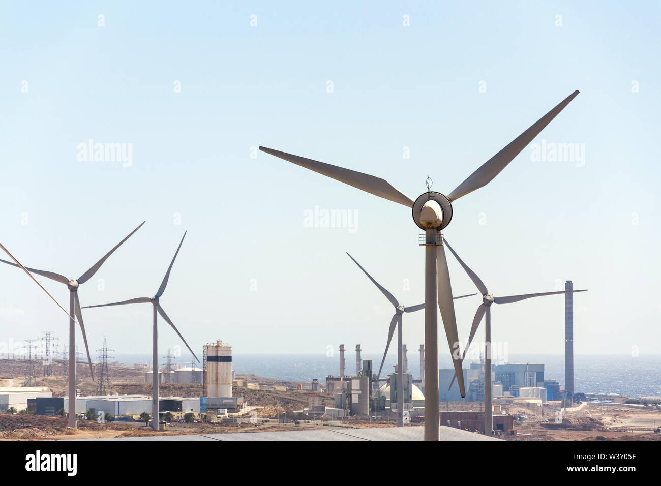 Les turbines éoliennes à blanc avec power station et mer en arrière-plan, paysage aride aux beaux jours de l'été, de l'électricité renouvelable durable concept Banque D'Images