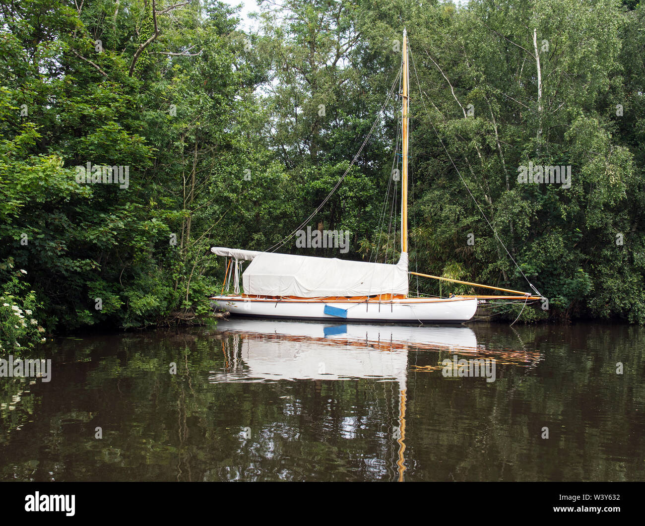 Une coque en bois traditionnel Norfolk Broads voile cruiser amarré à un site privé près de Womack Staithe, Ludham Norfolk reflète dans l'eau. Banque D'Images