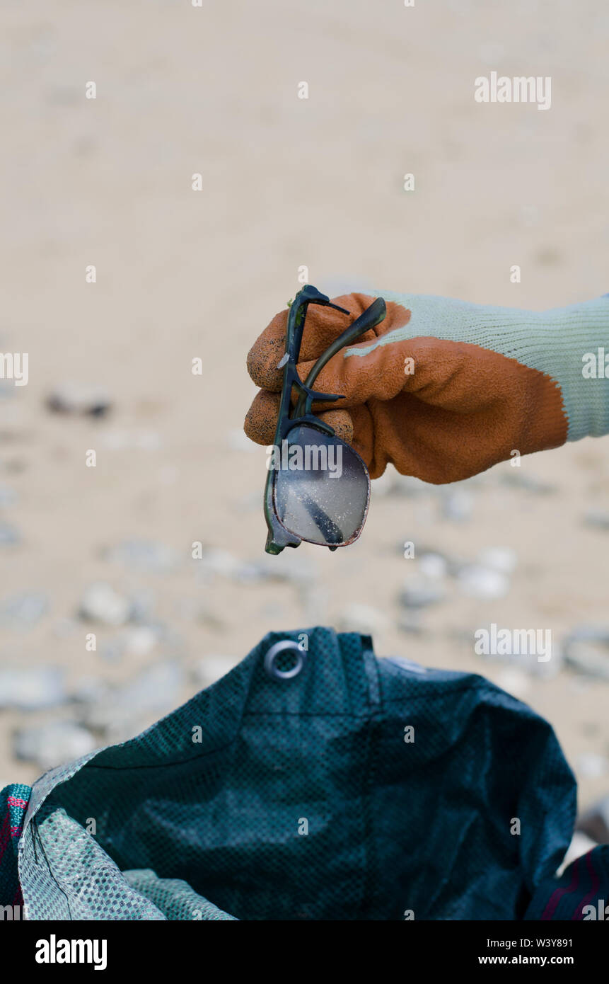 La main avec gant Orange Holding Broken Lunettes avec sac en plastique en arrière-plan on Beach Banque D'Images