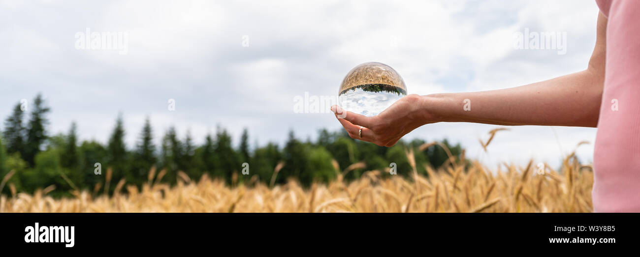 Femme tenant dans sa main une boule de cristal de nature permanente avec les champs et le ciel se reflétant dans la balle dans une image conceptuelle. Banque D'Images