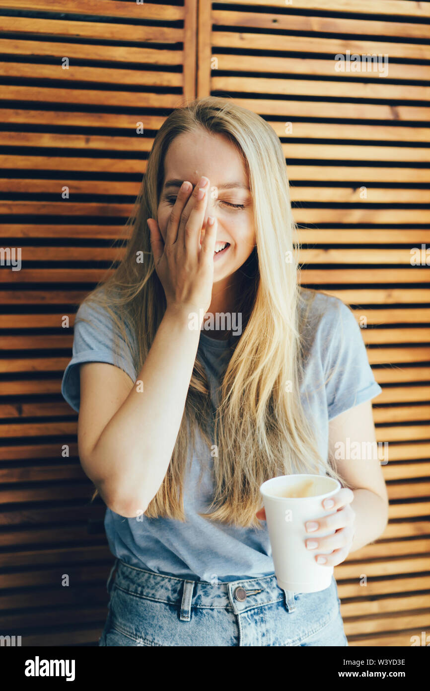 Un jeune blanc 30-year-old girl rire et lui couvre le visage avec sa main,  émotions naturelles, le mode de vie. Cheerful woman with a paper Coffee cup  sur un retour Photo Stock -