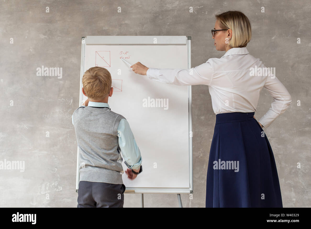 Un petit garçon portant des vêtements décontractés géométrie dessin figure sur le bureau tandis que son professeur lui corriger. Banque D'Images