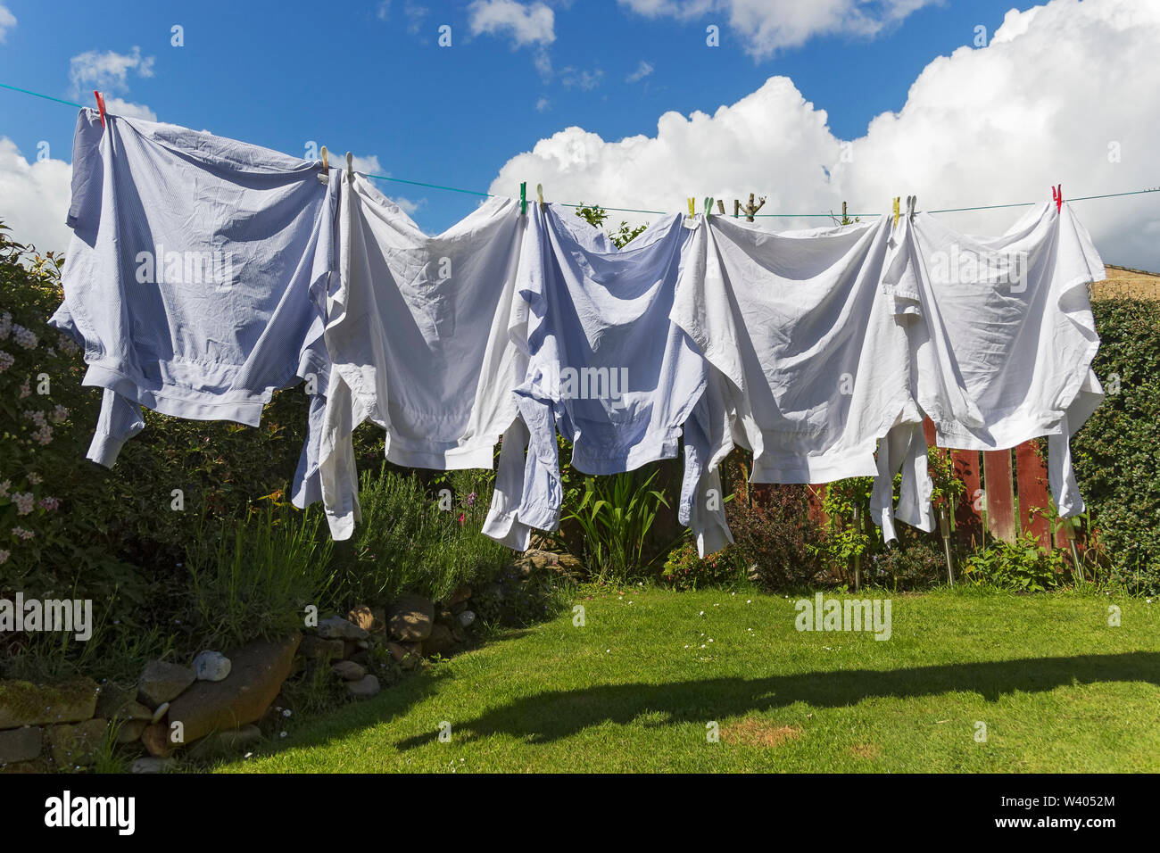 Shirts sèchent sur les lave-ligne dans UK jardin avec ciel bleu et nuages blancs moelleux. Banque D'Images