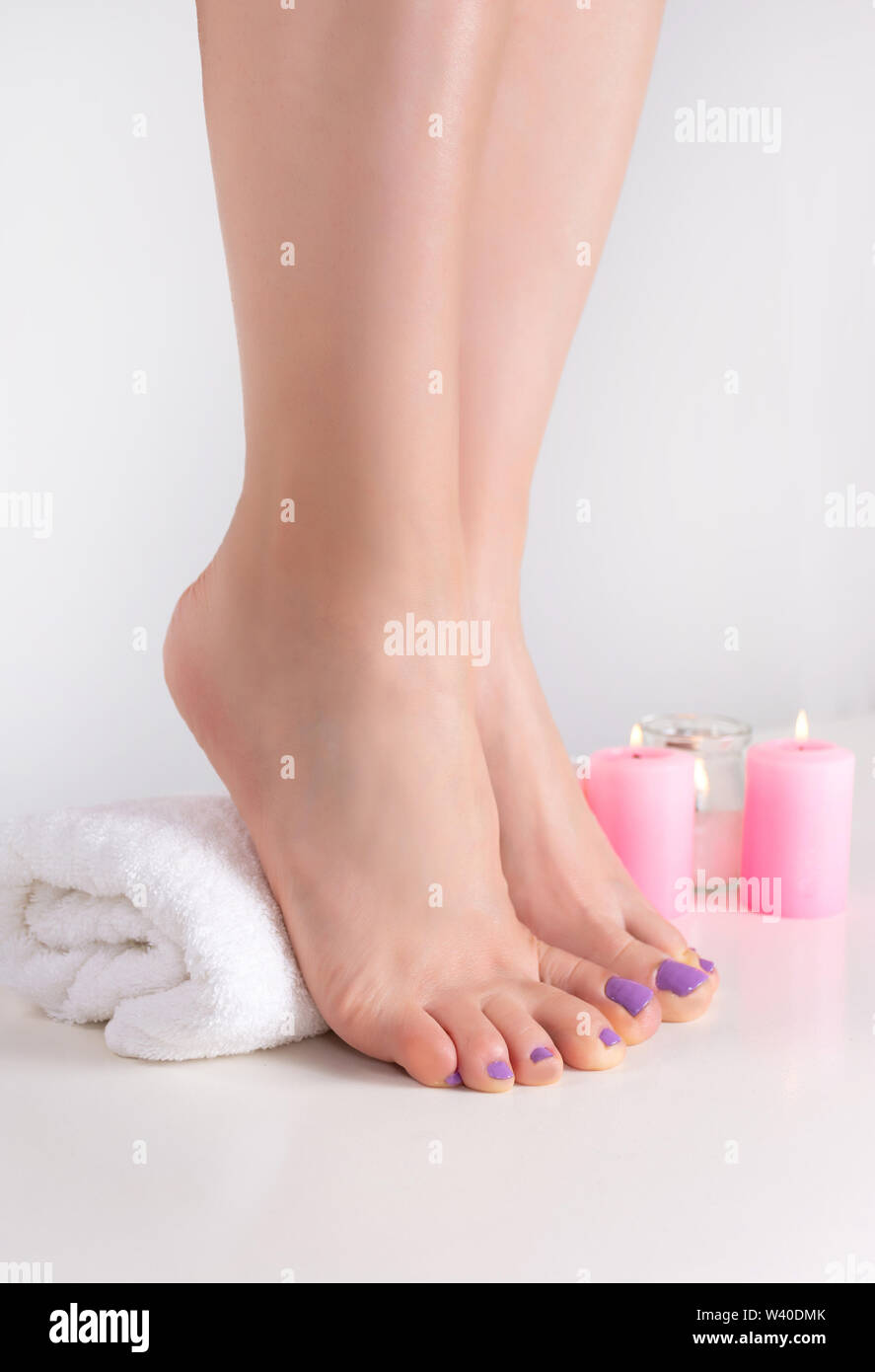 Les pieds avec des clous de couleur lilas polonais. Les jambes des femmes sur une serviette blanche et de décoration bougie dans salon de bien-être. Pédicure et manucure concept Banque D'Images