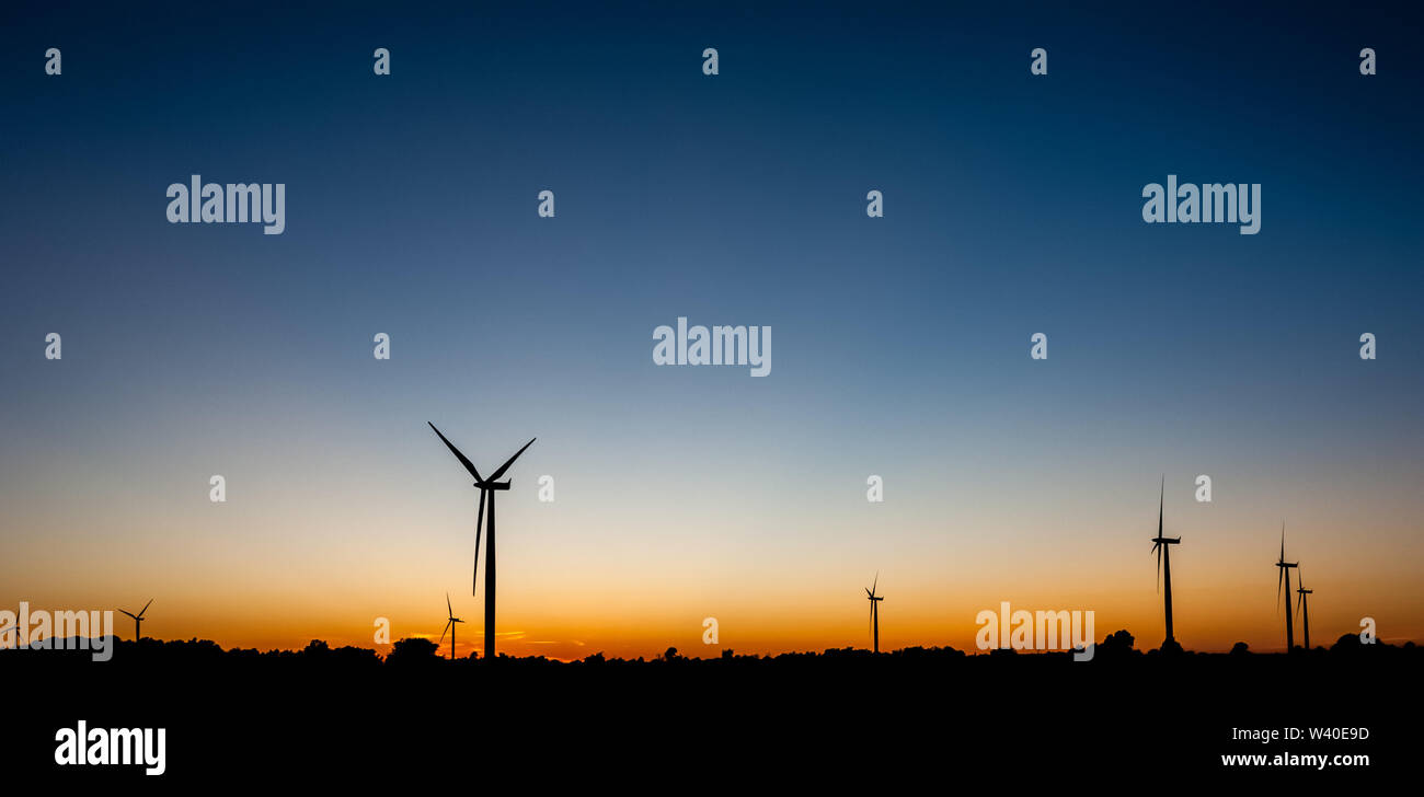 Silhouettes noires de plusieurs éoliennes contre orange et bleu ciel au crépuscule. Banque D'Images