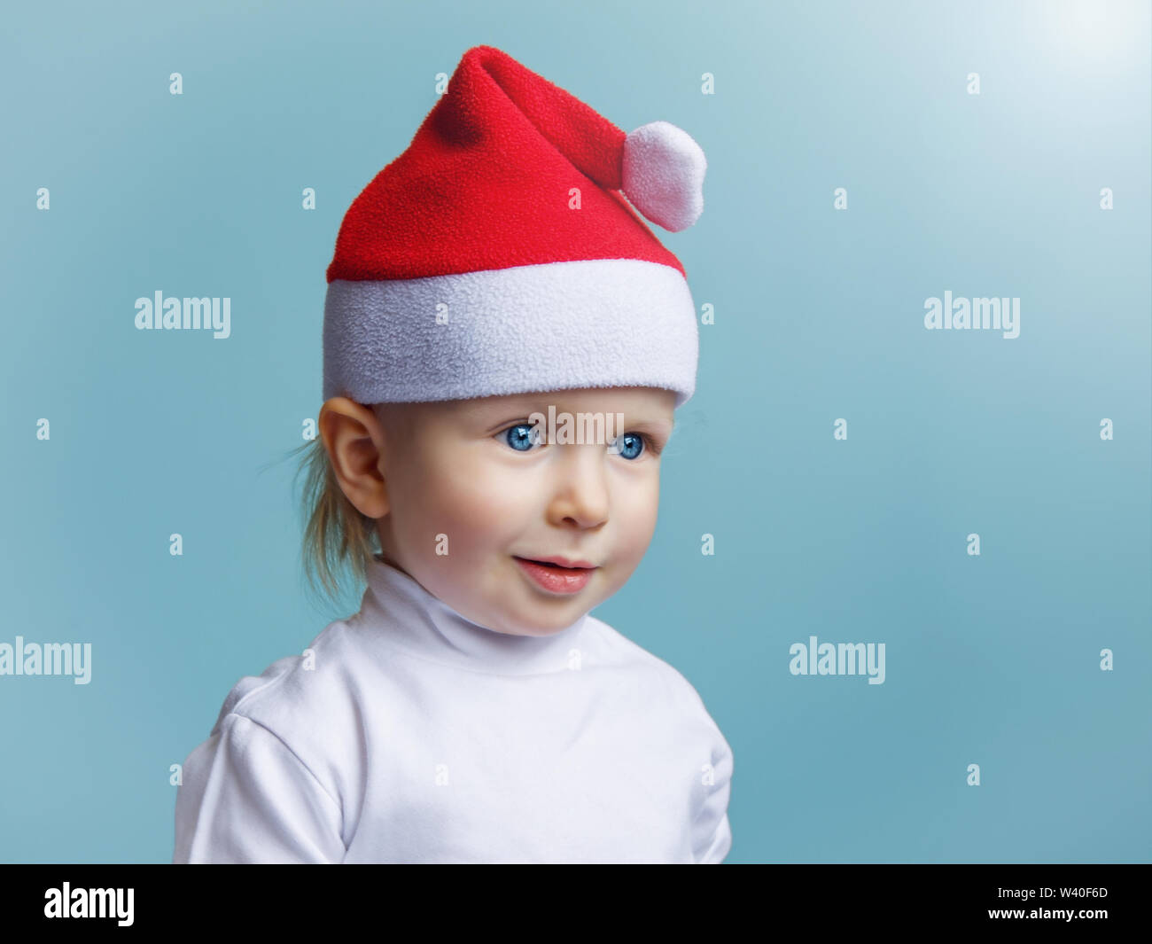 Closeup portrait of cute adorable belle Caucasian baby boy girl aux yeux bleus portant Santa Claus hat sur fond bleu clair. Nouvelle Année Christma Banque D'Images