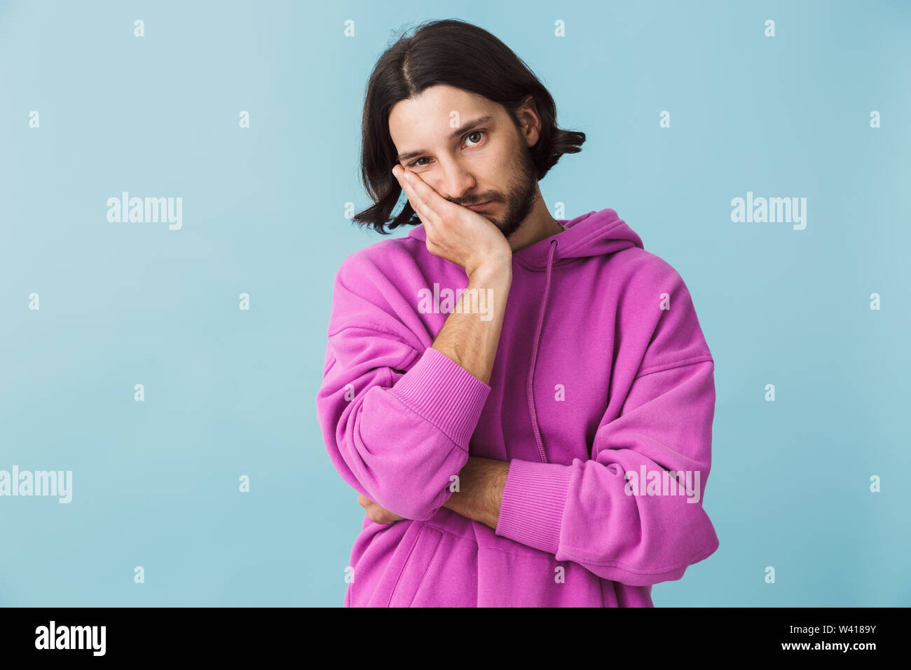Portrait d'une jeune brunette barbu homme portant hoodie isolés sur fond bleu Banque D'Images