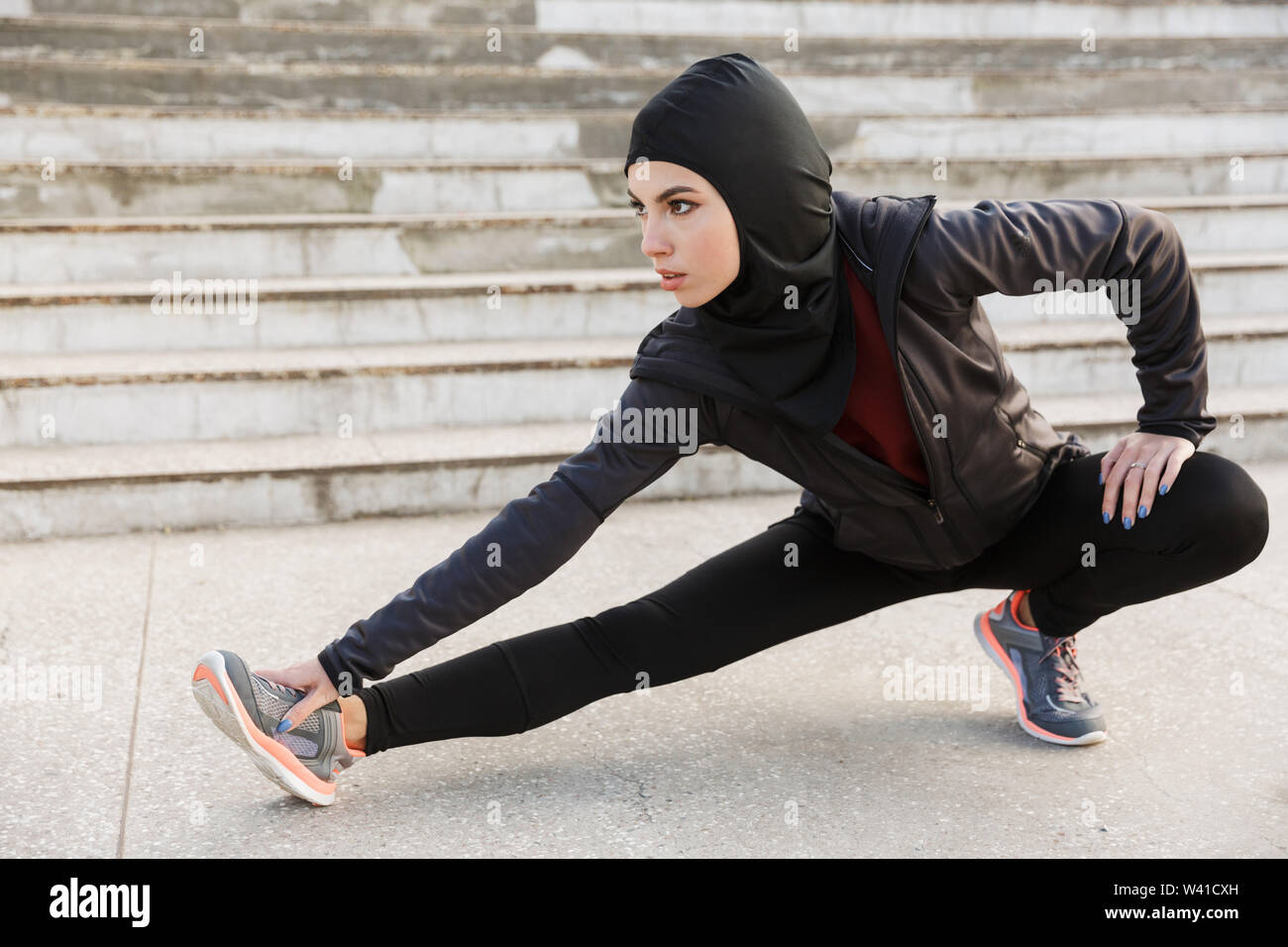 Image d'un jeune musulman concentré fitness sport femme vêtue de hijab et  vêtements sombres qui font du sport Les exercices d'étirement à l'extérieur  à la str Photo Stock - Alamy
