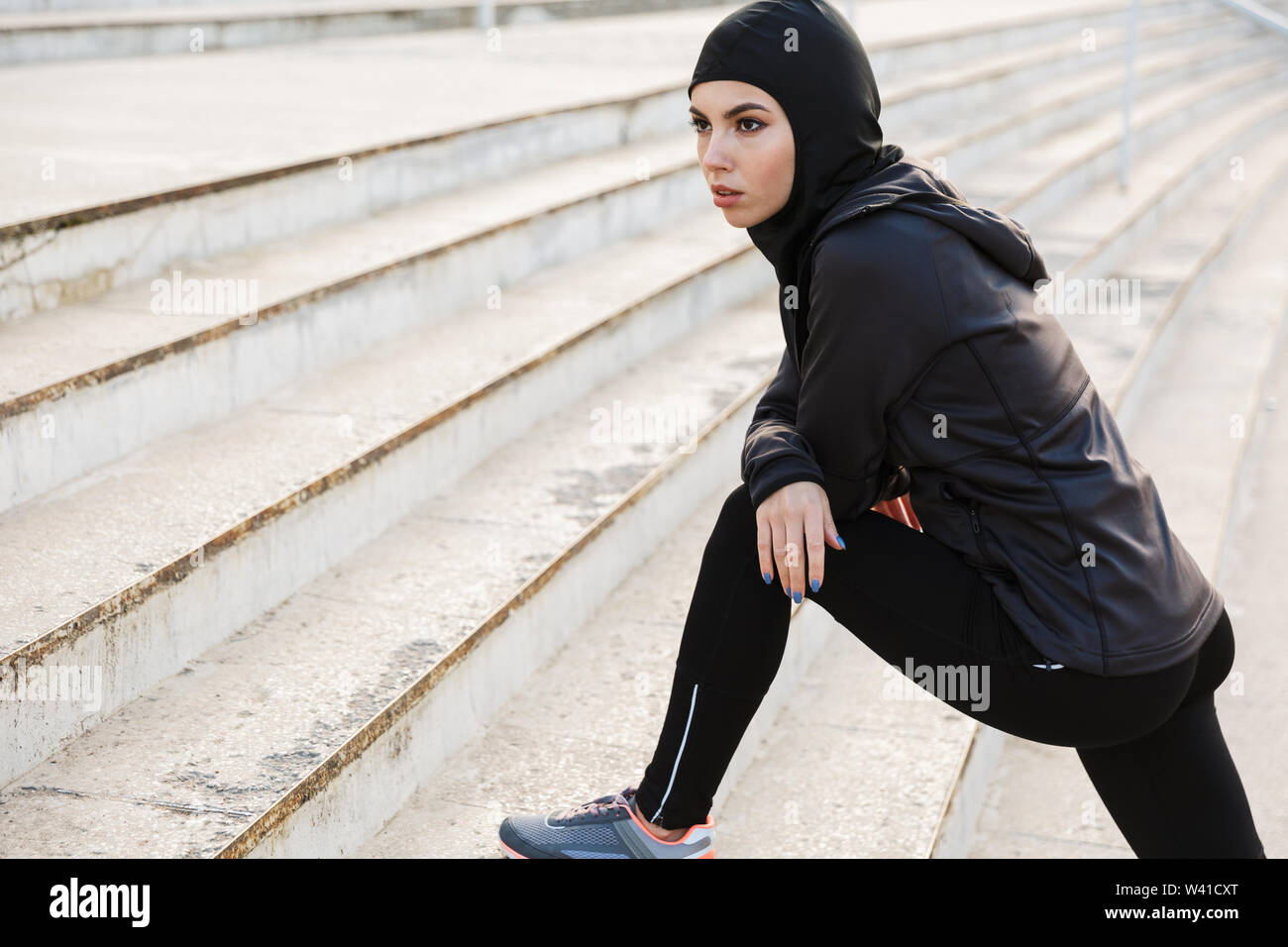 Image d'un jeune musulman concentré fitness sport femme vêtue de hijab et  vêtements sombres qui font du sport Les exercices d'étirement à l'extérieur  à la str Photo Stock - Alamy