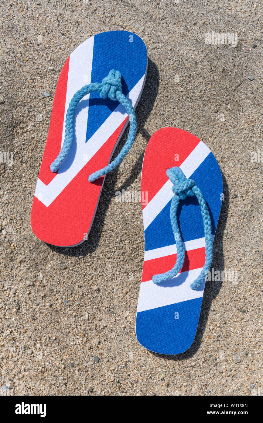 Drapeau GB / Union Jack flip-flops sur la plage de sable - pour 2021 la staycation britannique, les vacances à la maison, la staycation Cornwall, les vacances en bord de mer, les chaussures de flip-flop. Banque D'Images