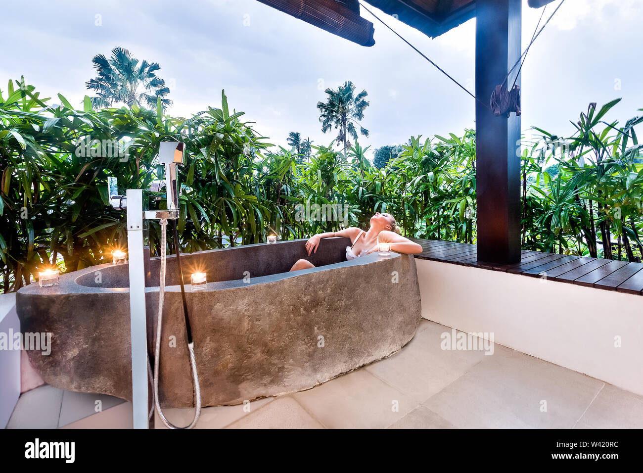 Jeune femme est de prendre un repos dans un bain à remous en pierre avec bougie clignotante autour d'elle et couvert de plantes vertes Banque D'Images