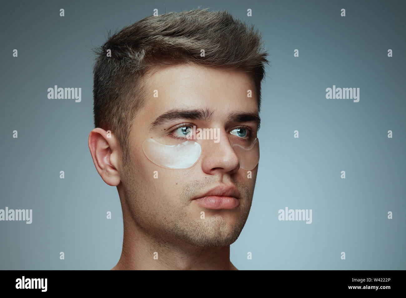 Close-up portrait of young man isolé sur fond studio gris. Visage masculin avec patches collagène sous les yeux. Concept de la santé des hommes et de la beauté, les soins de beauté, soins du corps et de la peau. Anti-vieillissement. Banque D'Images