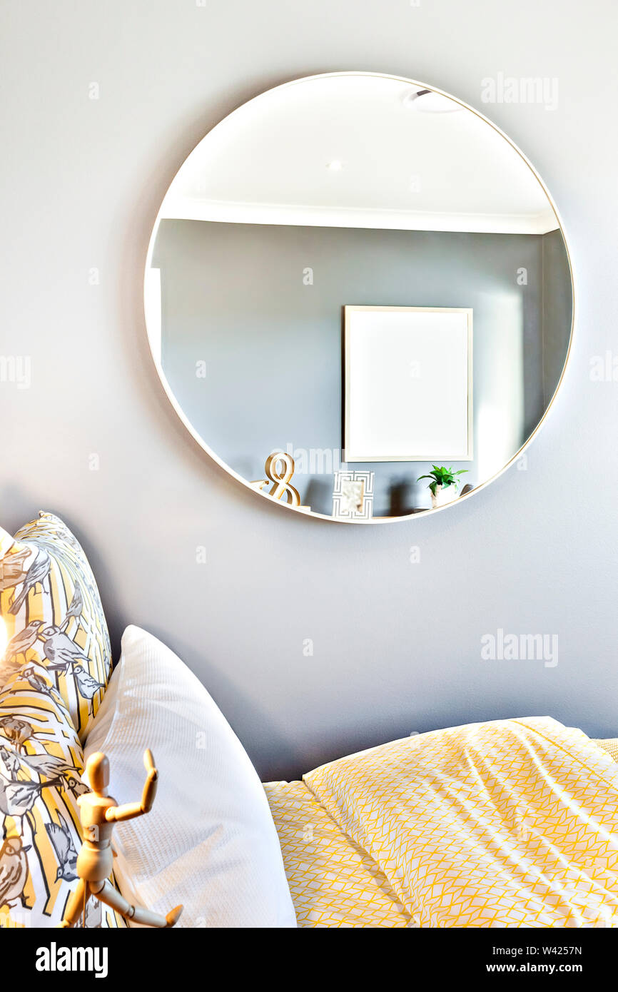 Miroir rond verre sur le mur à côté d'un lit avec draps et oreillers jaune,  la poupée en bois comme un humain à côté de tables de chevet sous le verre  Photo