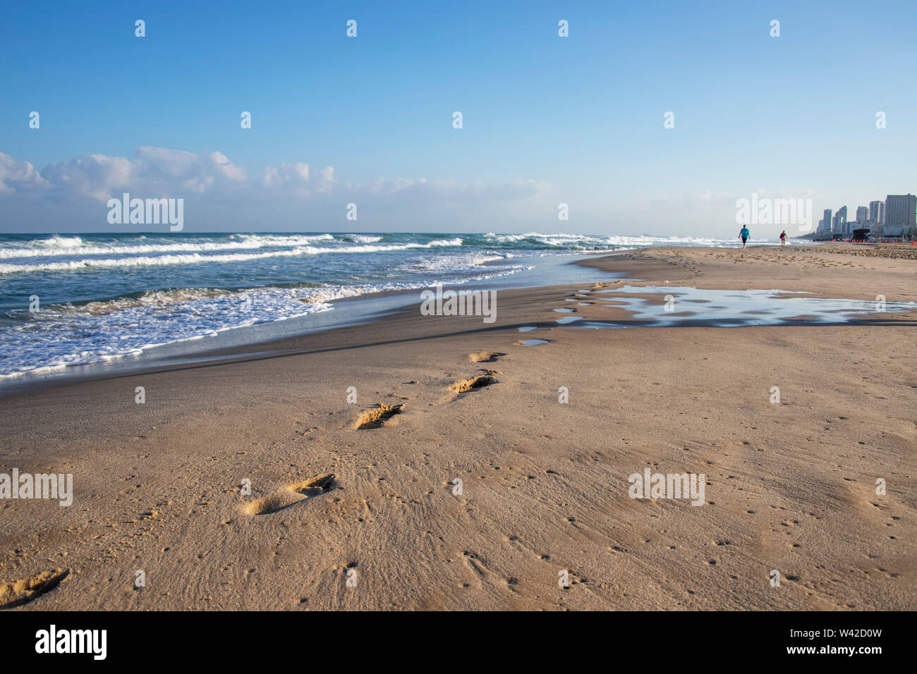 Empreintes de pas sur le sable d'une plage de la Méditerranée. Les vagues écumeuses et bâtiments à l'horizon. Israël Banque D'Images