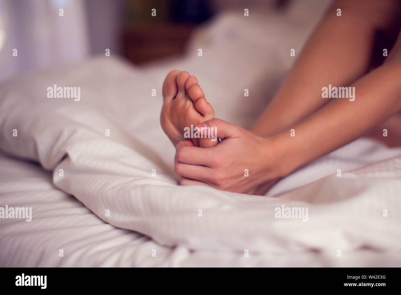 La douleur de pied femme assise sur le lit tenant ses pieds pieds douloureux d'avoir et d'étirement de la fatigue des muscles pour soulager la douleur. Les gens et la santé concept. Banque D'Images