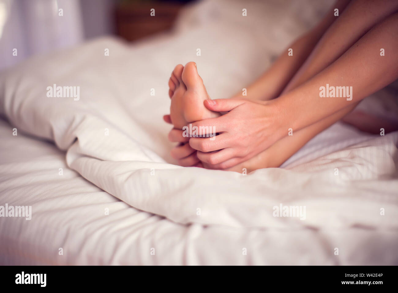 La douleur de pied femme assise sur le lit tenant ses pieds pieds douloureux d'avoir et d'étirement de la fatigue des muscles pour soulager la douleur. Les gens et la santé concept. Banque D'Images