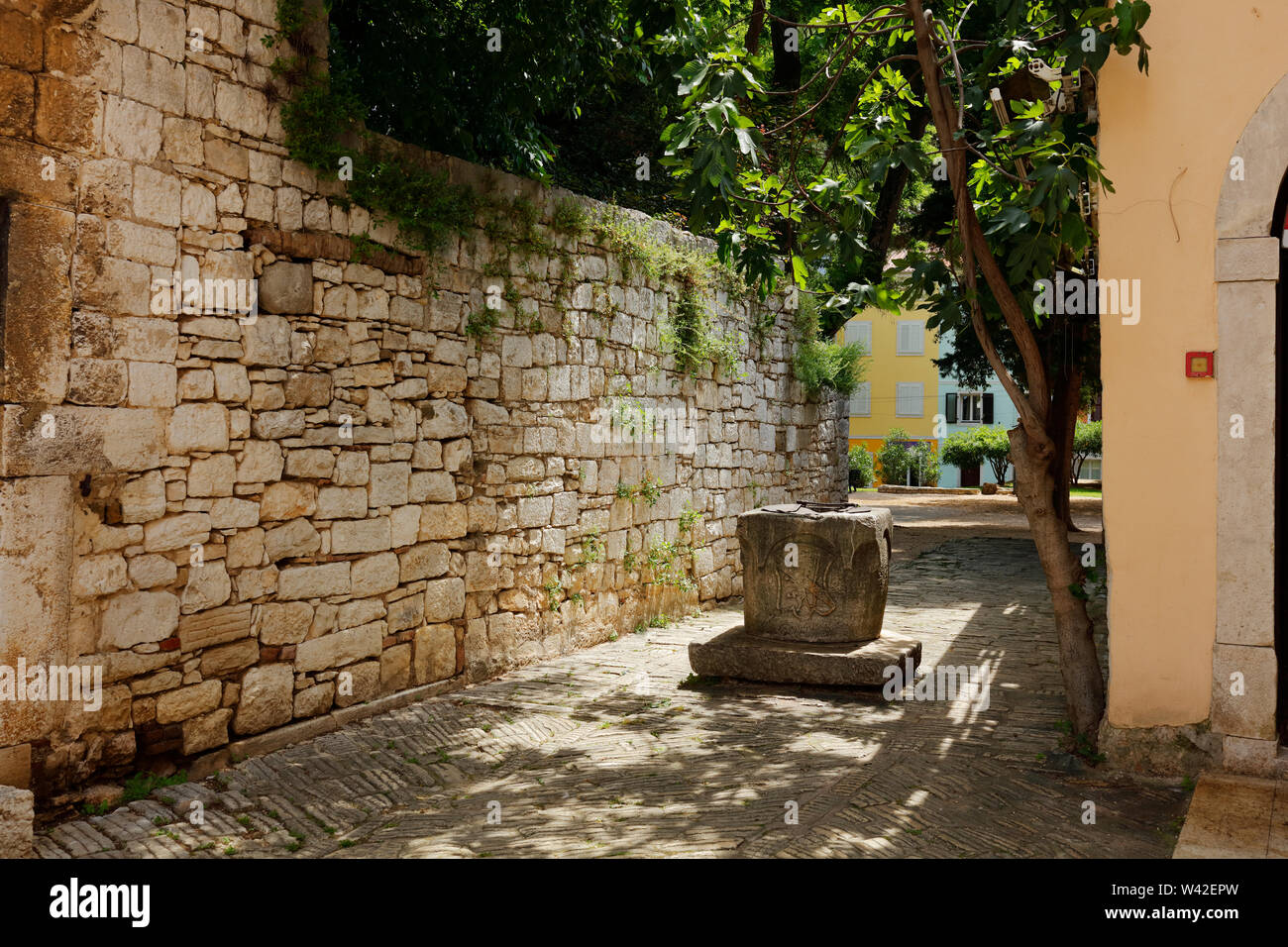 Vue sur une rue avec vieux mur en pierre et fontaine, Porec, Istrie, Croatie Banque D'Images