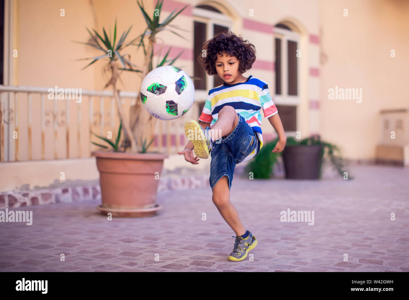 Petit garçon aux cheveux bouclés avec ballon de soccer extérieur. Les enfants et de divertissement concept Banque D'Images