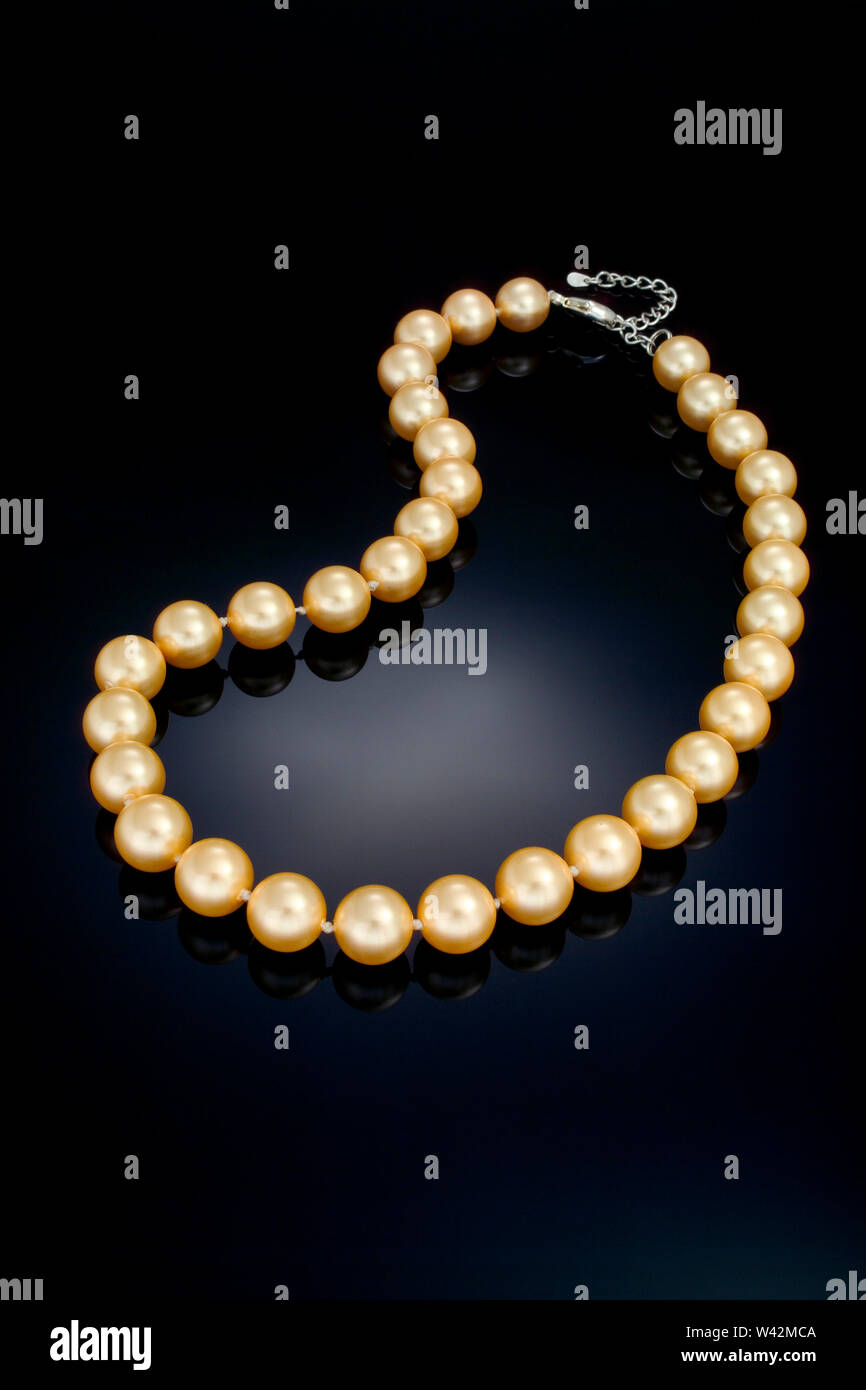 Une seule mèche couleur or collier de perle se trouve sur un fond noir  refective Photo Stock - Alamy