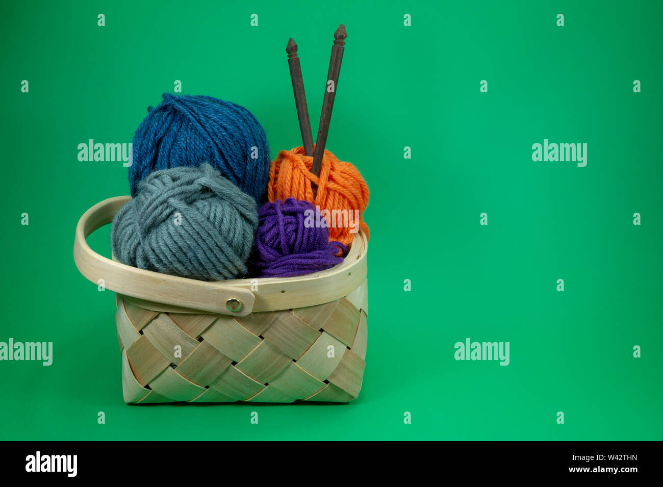 L'artisanat et de l'aiguille de concept - panier en osier avec boules colorées de la laine et des aiguilles à tricoter sur fond vert avec copie gratuite savs Banque D'Images