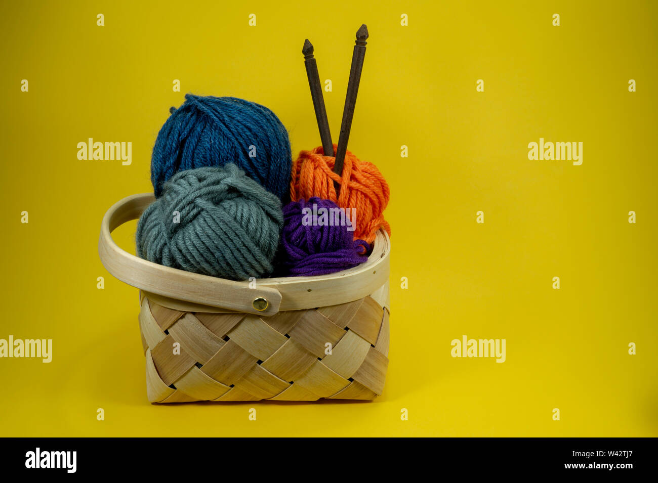 L'artisanat et de l'aiguille de concept - panier en osier avec boules colorées de la laine et des aiguilles à tricoter sur fond jaune avec copie gratuite spa Banque D'Images