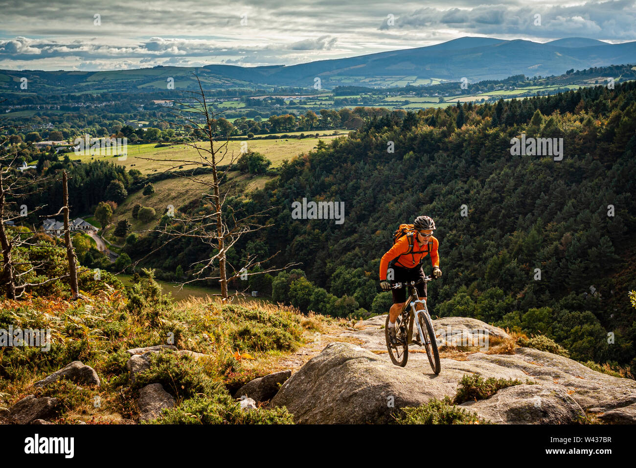Un vélo de montagne équitation une dalle de roche avec montagnes de Wicklow et ciel dramatique derrière. Banque D'Images