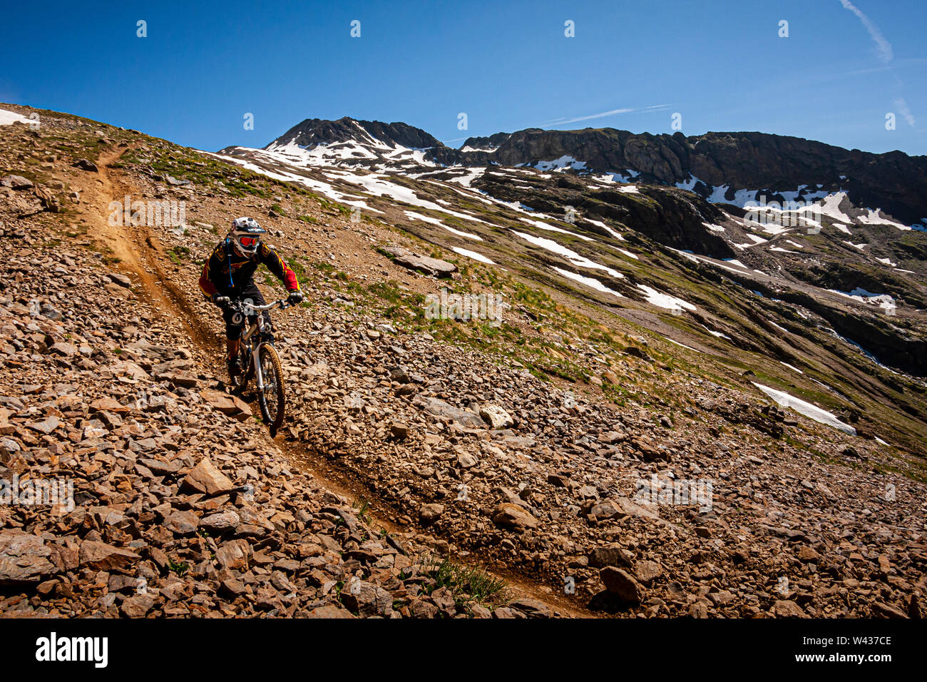 Un vélo de montagne équitation un étroit sentier alpin à travers un champ de roches avec des plaques de neige et les montagnes rocheuses être Banque D'Images