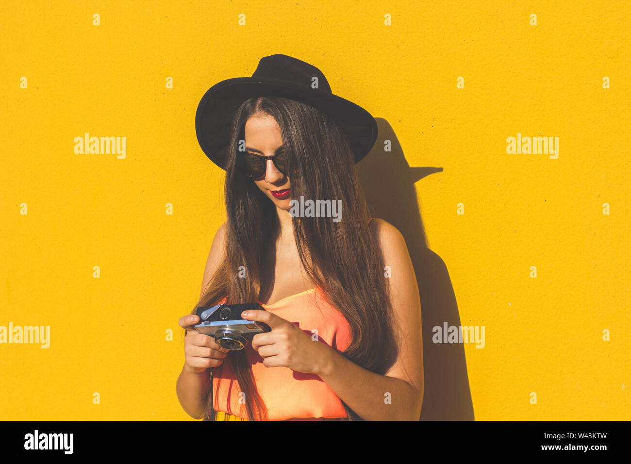 Hipster girl wearing sunglasses à la mode et à l'aide d'un appareil photo vintage Banque D'Images
