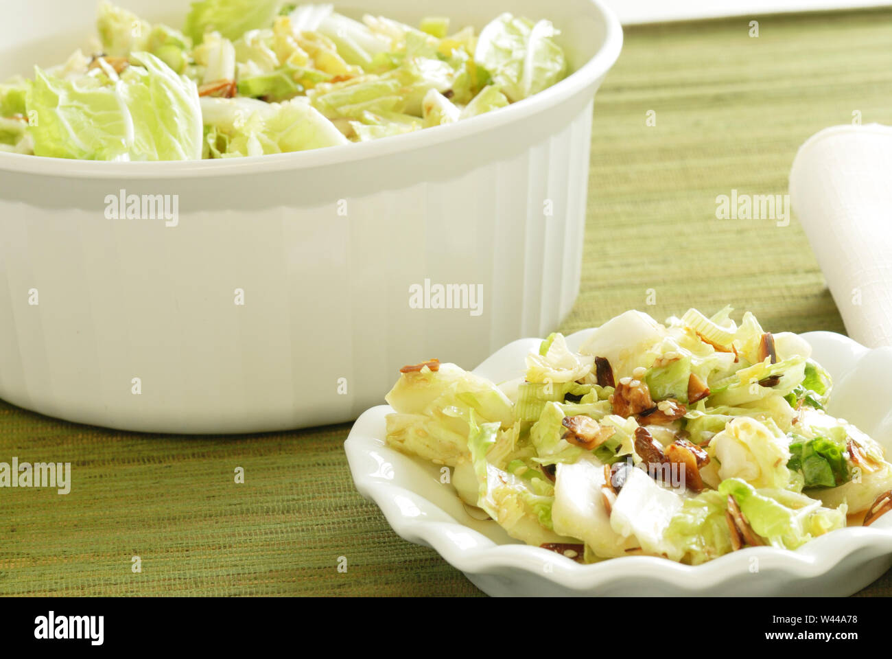 Un bol de salade de chou faite de chou nappa et parsemé de graines de sésame grillées et amandes tranchées, avec une portion individuelle au premier plan Banque D'Images