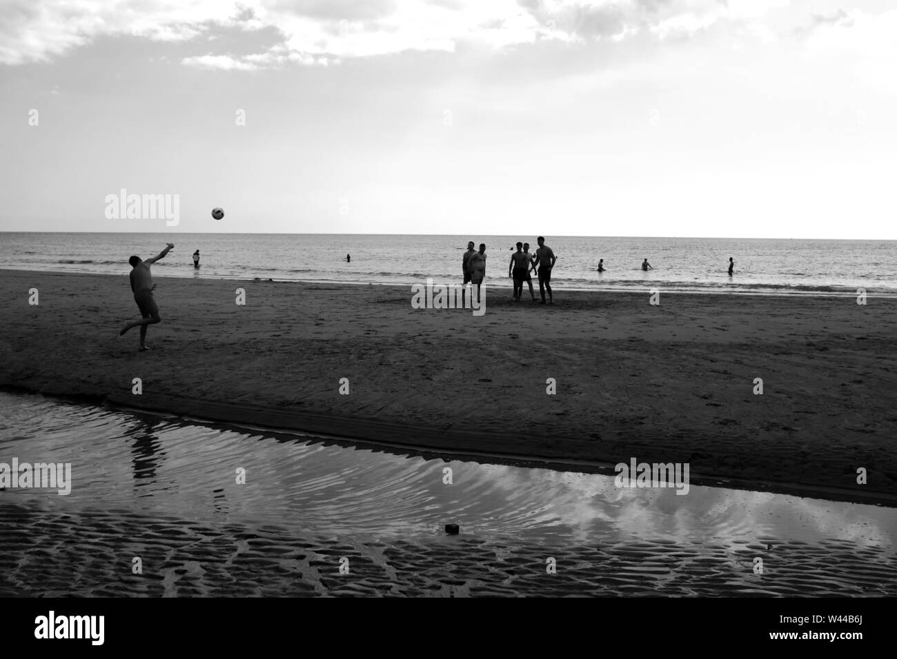 Un groupe de jeunes hommes jouent au football sur la plage de sable à marée basse. L'un d'eux est de lancer la balle pour les autres Banque D'Images