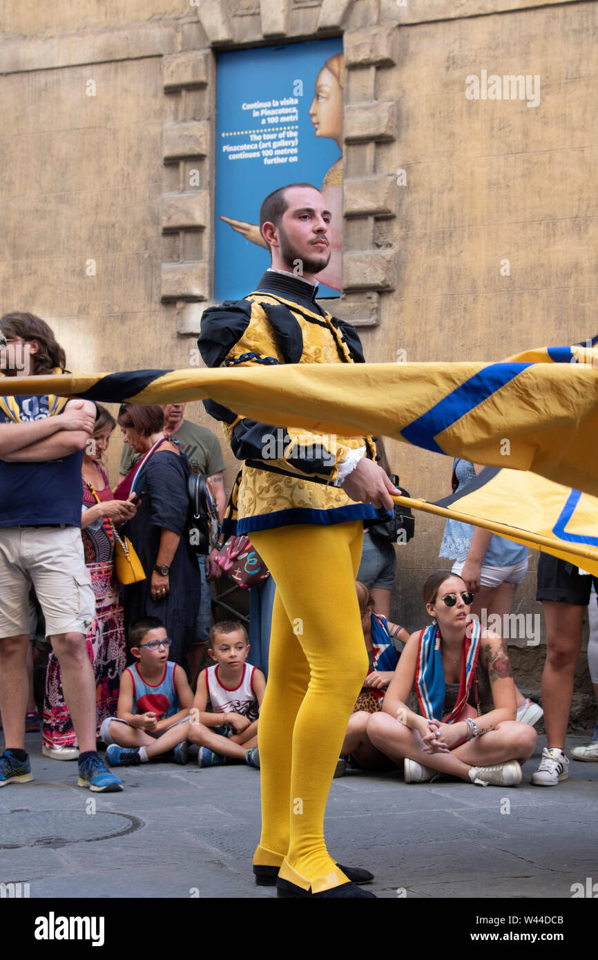 Jeune homme en costume médiéval vagues un drapeau tout en marchant à travers les rues de Sienne, Italie à l'assemblée annuelle de chevaux Palio historique et défilé Banque D'Images