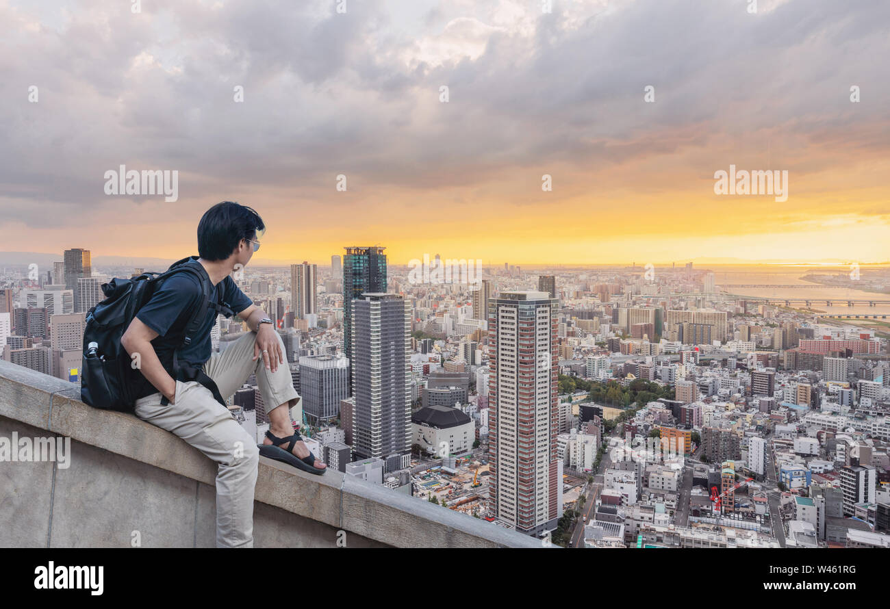 Sac à dos avec un homme à la vue sur la ville au coucher du soleil en été dans Banque D'Images