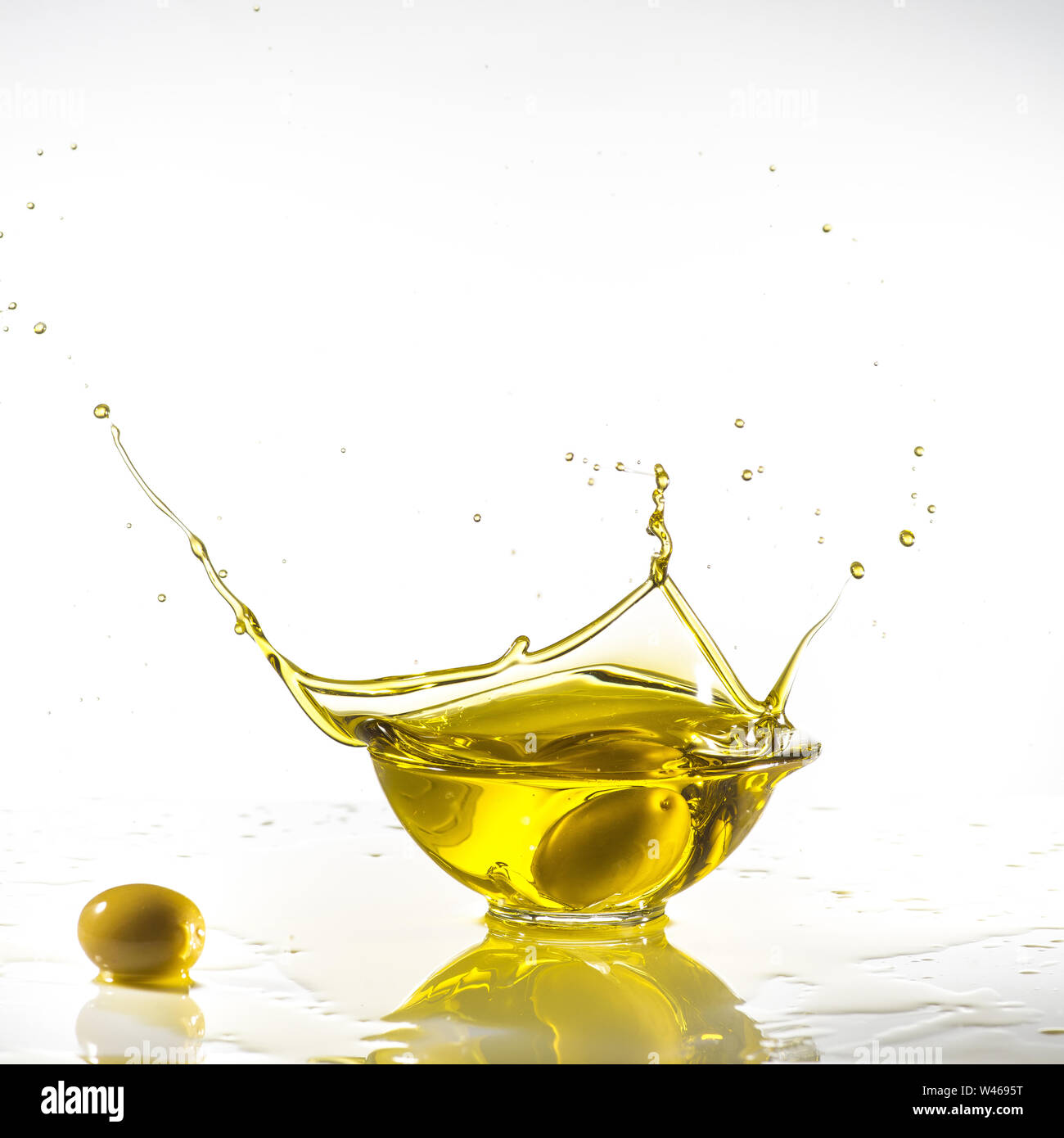 Quelques olives vertes tombent dans un bol rempli d'huile d'olive avec splash. Fond blanc Banque D'Images