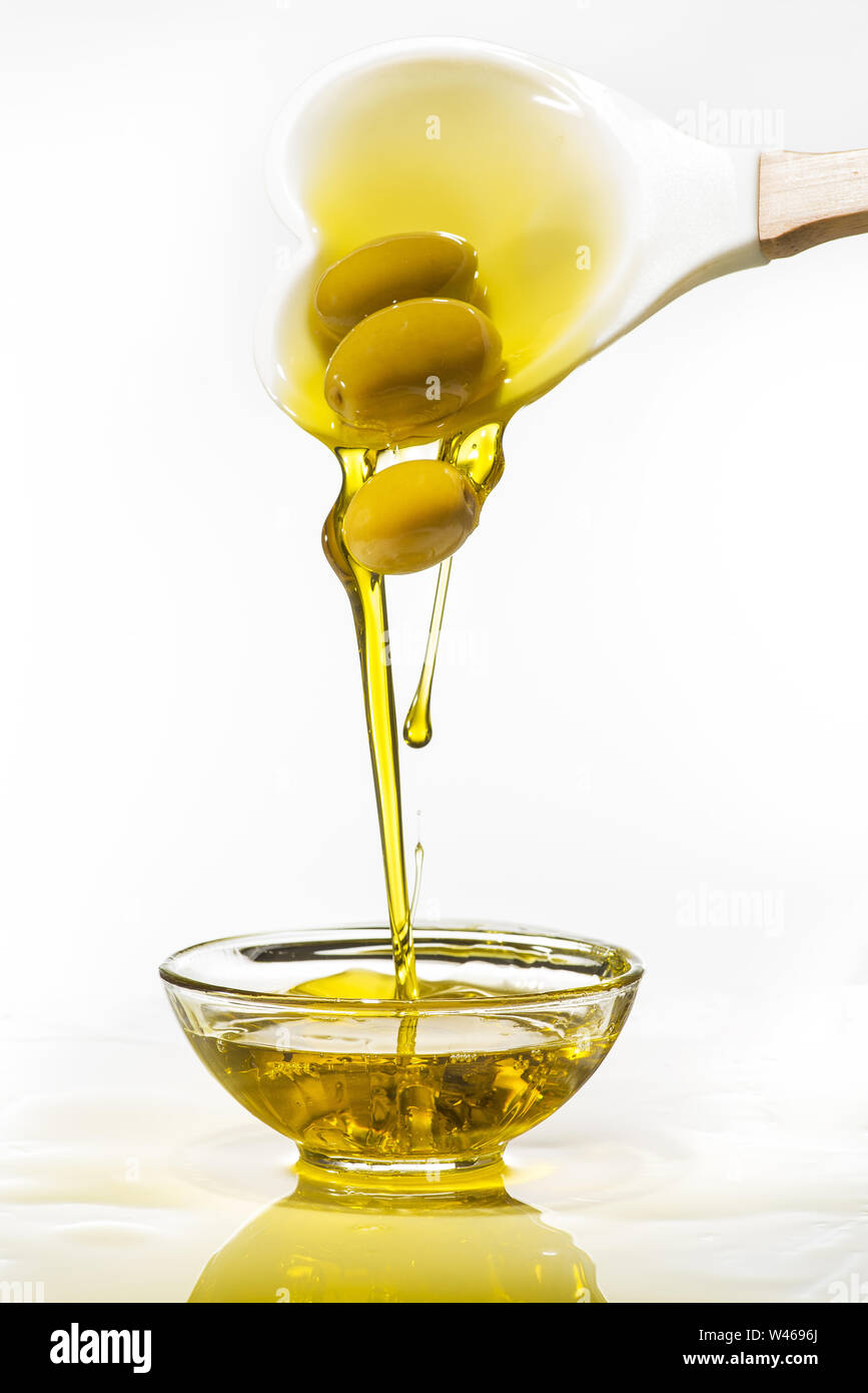 À partir d'une cuillère, avec la forme d'un coeur, quelques olives vertes tombent dans un bol rempli d'huile d'olive avec splash. Fond blanc Banque D'Images