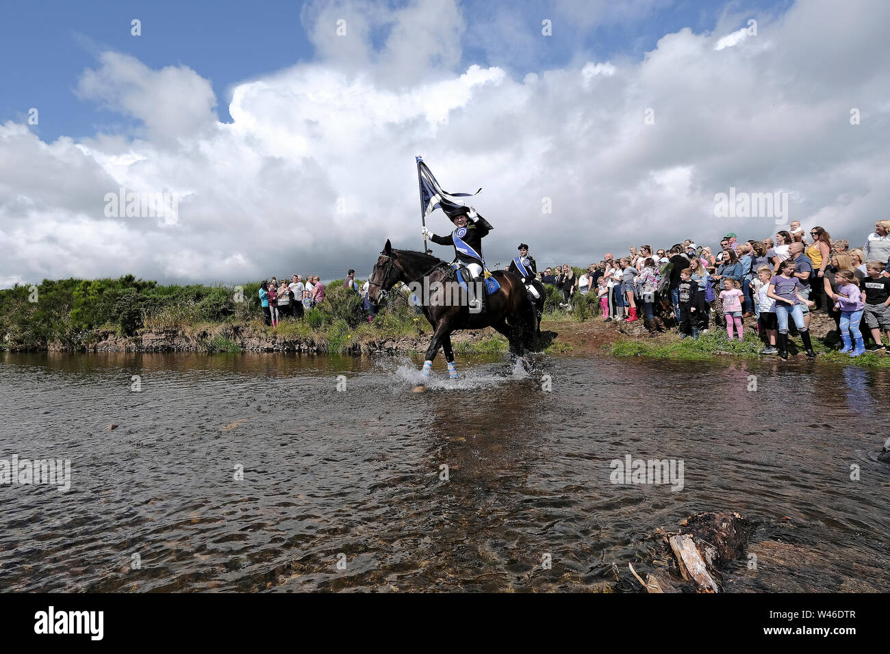 Kelso, Ecosse, Royaume-Uni. 20 juillet 2019. Semaine civique Kelso - at Yetholm Ride out, Kelso. Laddie Kelso Mark Henderson porte le drapeau de la ville (Standard) comme il l'Bowmont Ford d'eau devant la montée forte 200 cavalcade avec Sean RHM Crochet (2018 KL), Craig Logan (2017 KL), sur le trajet vers Whitehouse Country House Samedi 20 juillet 2019. (Crédit : Rob Gray ) Crédit : Rob Gray/Alamy Live News Banque D'Images