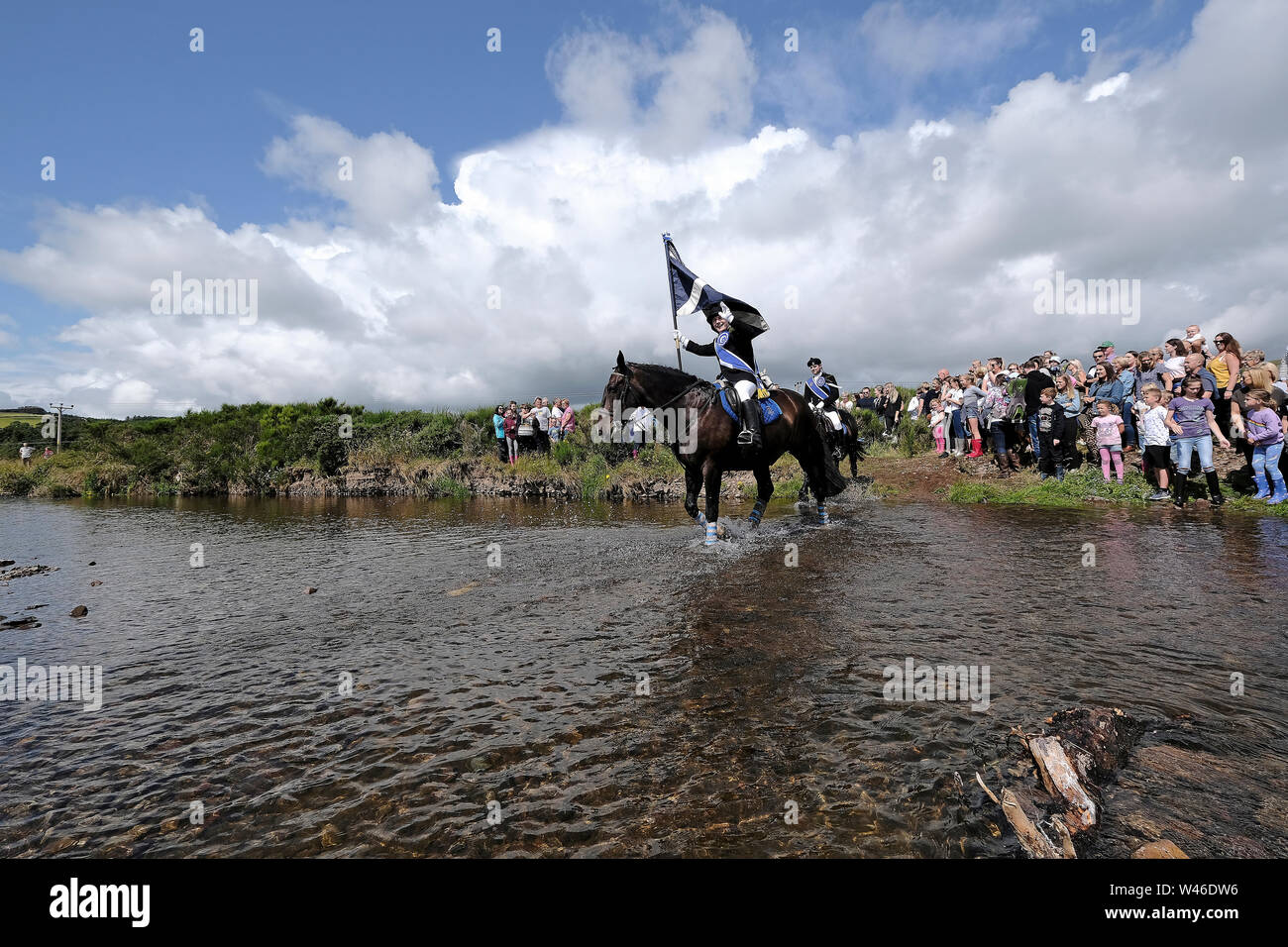 Kelso, Ecosse, Royaume-Uni. 20 juillet 2019. Semaine civique Kelso - at Yetholm Ride out, Kelso. Laddie Kelso Mark Henderson porte le drapeau de la ville (Standard) comme il l'Bowmont Ford d'eau devant la montée forte 200 cavalcade avec Sean RHM Crochet (2018 KL), Craig Logan (2017 KL), sur le trajet vers Whitehouse Country House Samedi 20 juillet 2019. (Crédit : Rob Gray ) Crédit : Rob Gray/Alamy Live News Banque D'Images