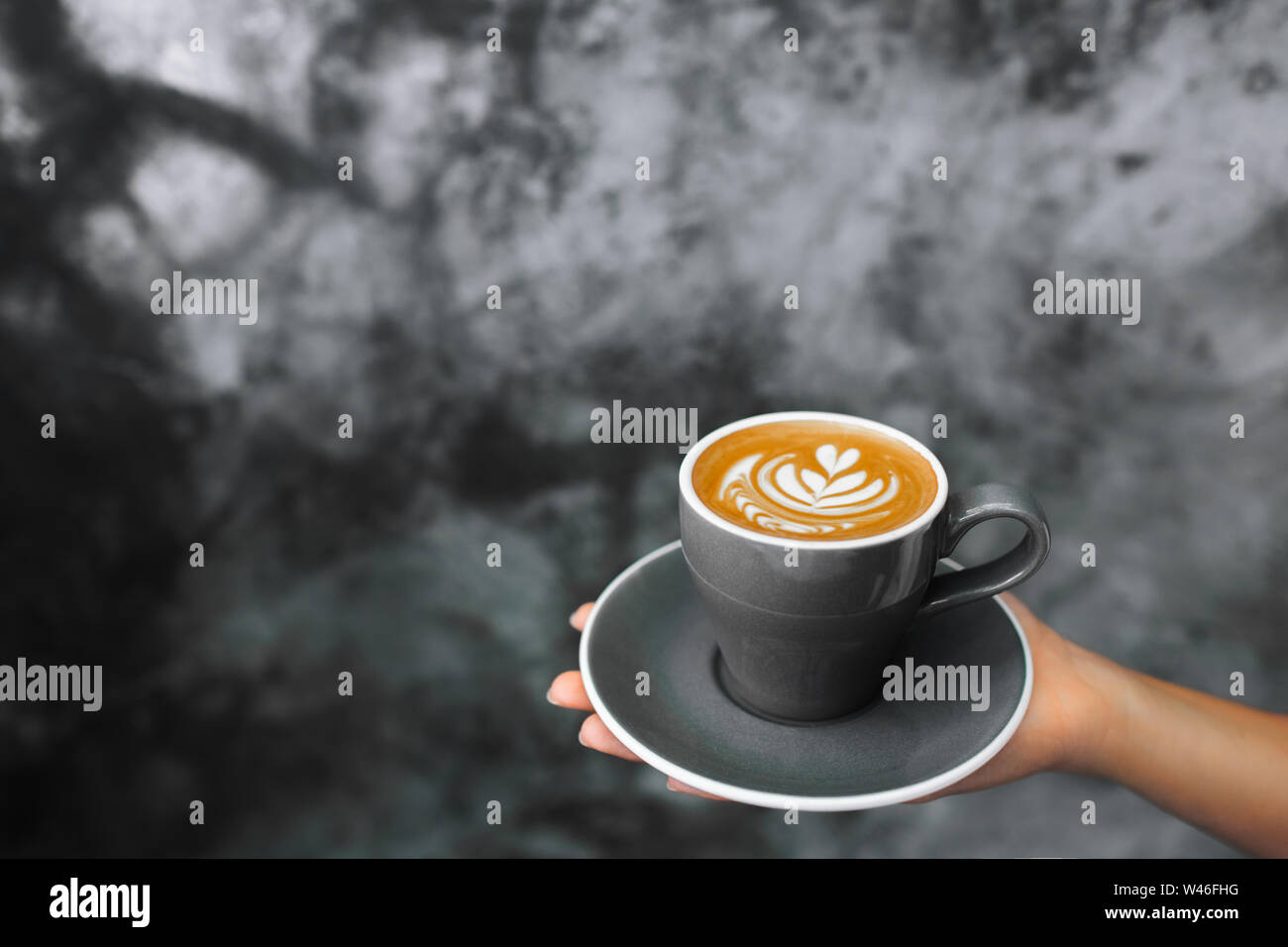 Femme tenant en main tasse de Cappuccino gris sur fond de ciment Mur de béton gris texturé. Hipster tendance design cafe. Banque D'Images